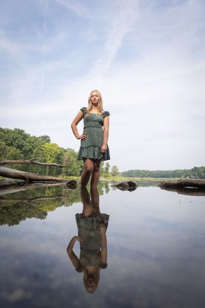 Person standing on a wooden dock at a serene lake creates mirror reflection in calm waters during summer.