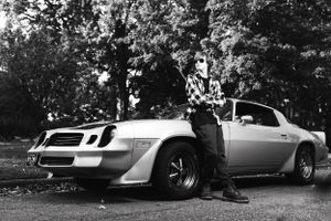 A classic Chevrolet Camaro Z28 muscle car in silver with wide tires parked in a wooded setting.