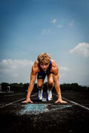 Athlete in starting position on track preparing for sprint race at outdoor running track under blue sky.