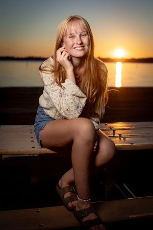 Portrait at sunset of someone sitting on a dock by a lake wearing a sweater and denim shorts.
