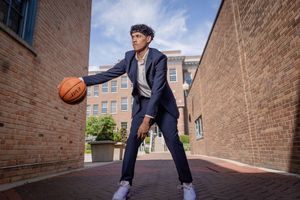 Basketball player dribbles in an alley between brick buildings wearing navy blue athletic wear.