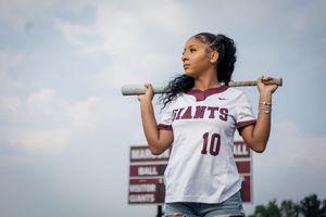 A baseball player in a Giants jersey number 10 holds a bat across their shoulders against a cloudy sky.