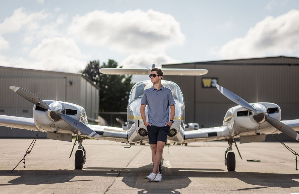 A person stands between two small private aircraft on a sunny day at an airport.