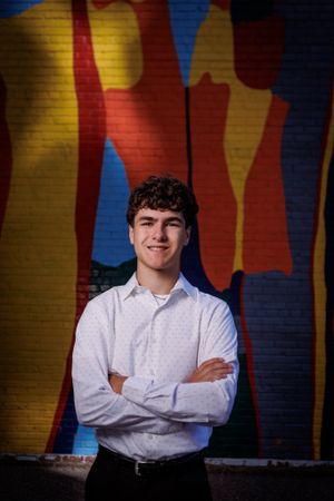 A portrait against a colorful abstract mural with yellow, red and blue shapes painted on a wall.