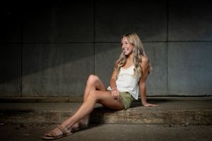 Portrait of person in white top posing against industrial wall with dramatic lighting.