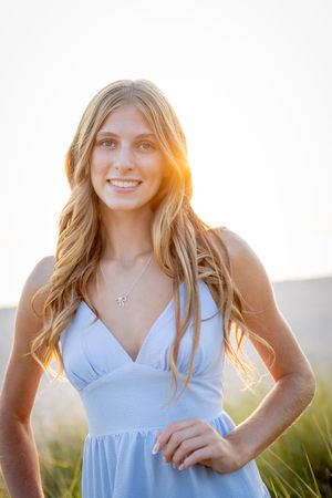 A person in a light blue dress poses outdoors during golden hour with sunlight creating a warm backlit glow.