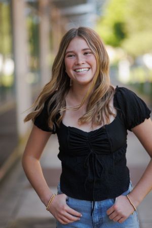 Casual outdoor portrait featuring a smiling person in a black puff sleeve top and blue jeans against a blurred background.