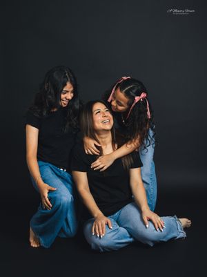 Three women in matching black tops and jeans share a joyful moment together in a professional studio portrait.