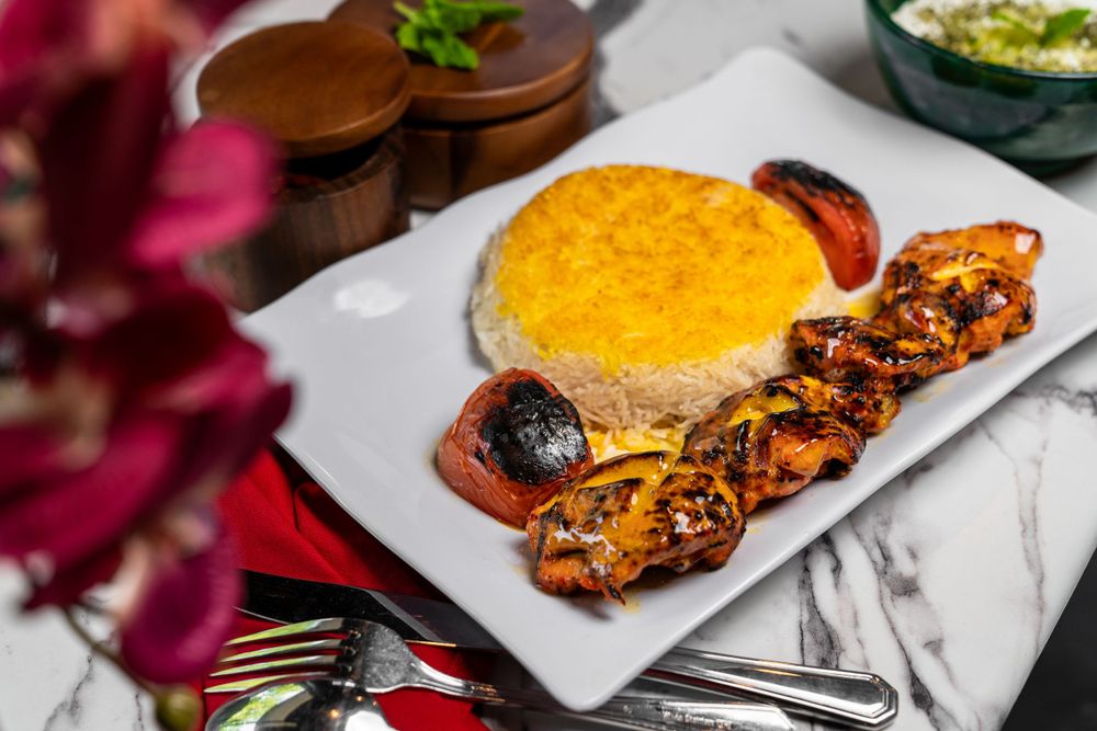 Grilled meat dish served with yellow rice and roasted vegetables on white plate.