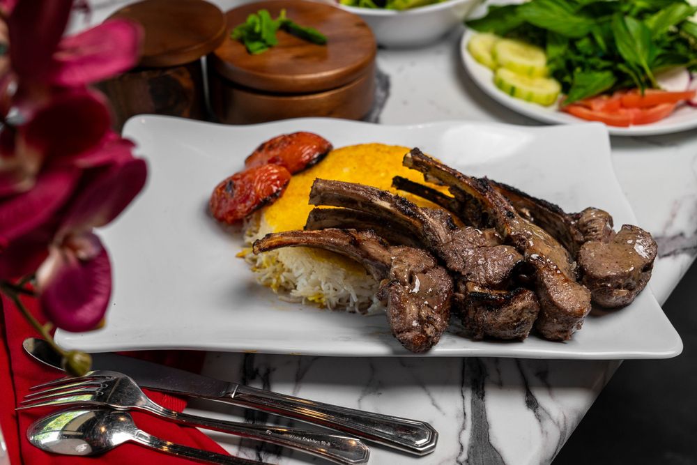 Sliced steak dinner with roasted vegetables served on white plate with elegant place setting.