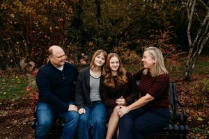 A family wearing coordinating blue and burgundy outfits poses together in an autumn forest setting.