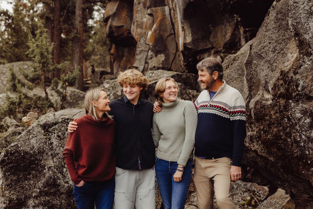 A group poses for outdoor family photos among rocky cliffs in warm autumn lighting.