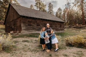Rustic barn engagement photoshoot in a forest setting during golden hour with pine trees in the background.