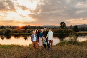 A group stands together by a serene lake at sunset with golden light illuminating the landscape and clouds above.