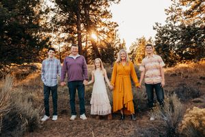 Group of people standing together in a field at sunset with golden sunlight filtering through trees.