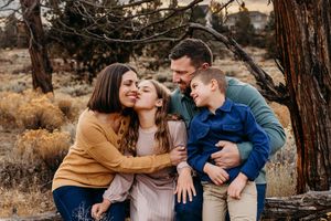 A family shares joyful laughter together while sitting outdoors among pine trees in autumn.