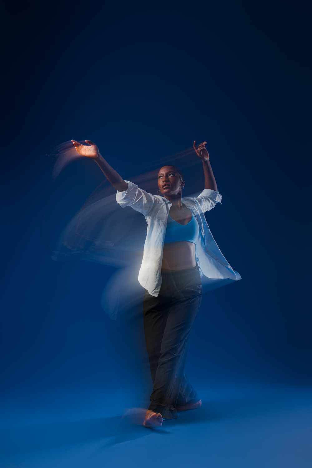 Dancer in white shirt and dark pants creates motion blur effect while performing against blue background.