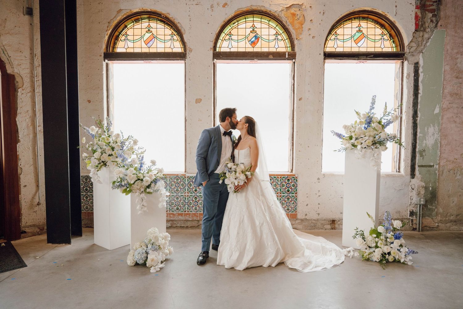 Wedding party posing in an elegant venue with arched windows and rustic architectural details.