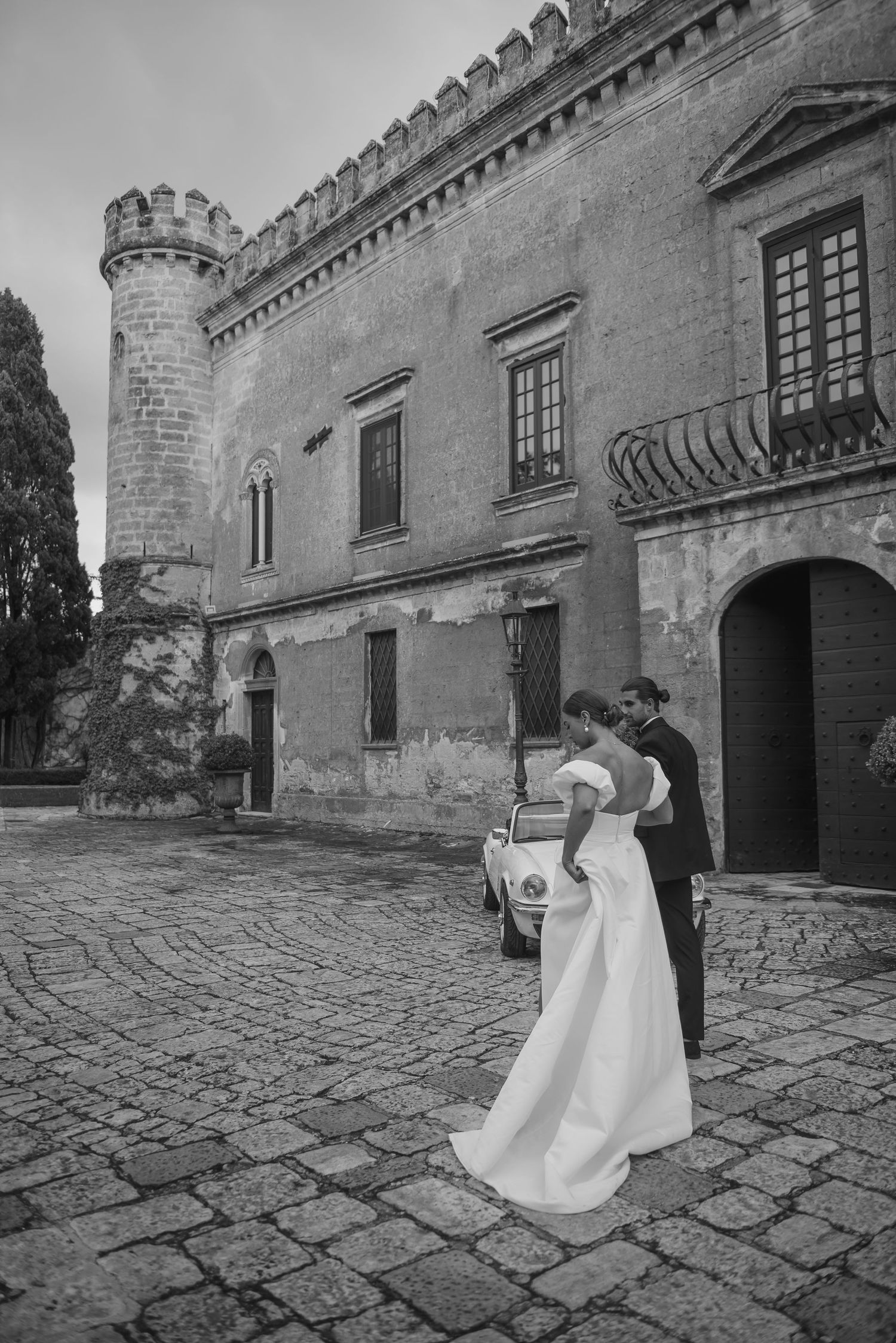 A couple shares an elegant dance moment on a cobblestone courtyard in front of a historic castle with stone turrets.