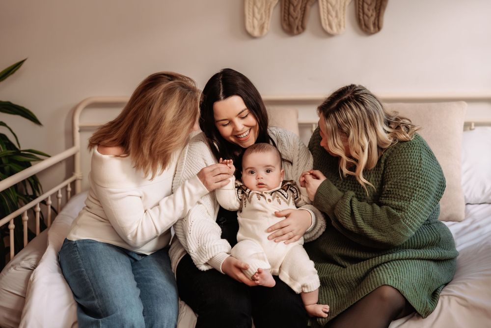 Intimate family moment on a white bed with soft knit socks hanging on the wall.