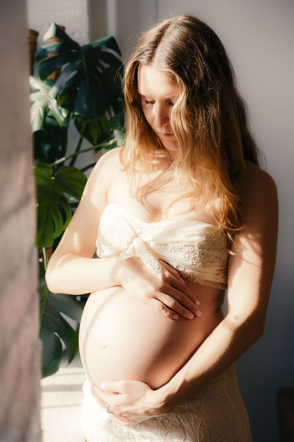 Maternity photoshoot series showing pregnant woman in white lace top against neutral background.