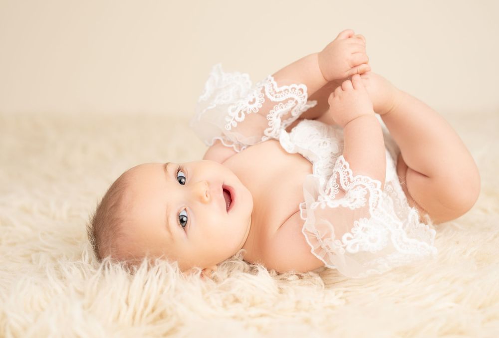 Adorable baby girl lying on fur blanket holding her feet during milestone studio session in Etobicoke