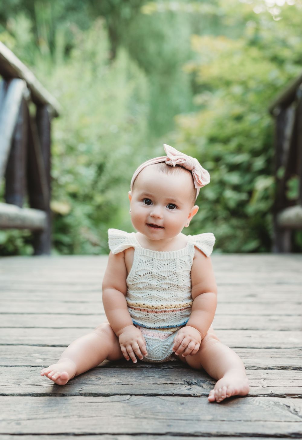 One year old girl sitting on a bridge with big smile during outdoor first birthday session in Etobicoke
