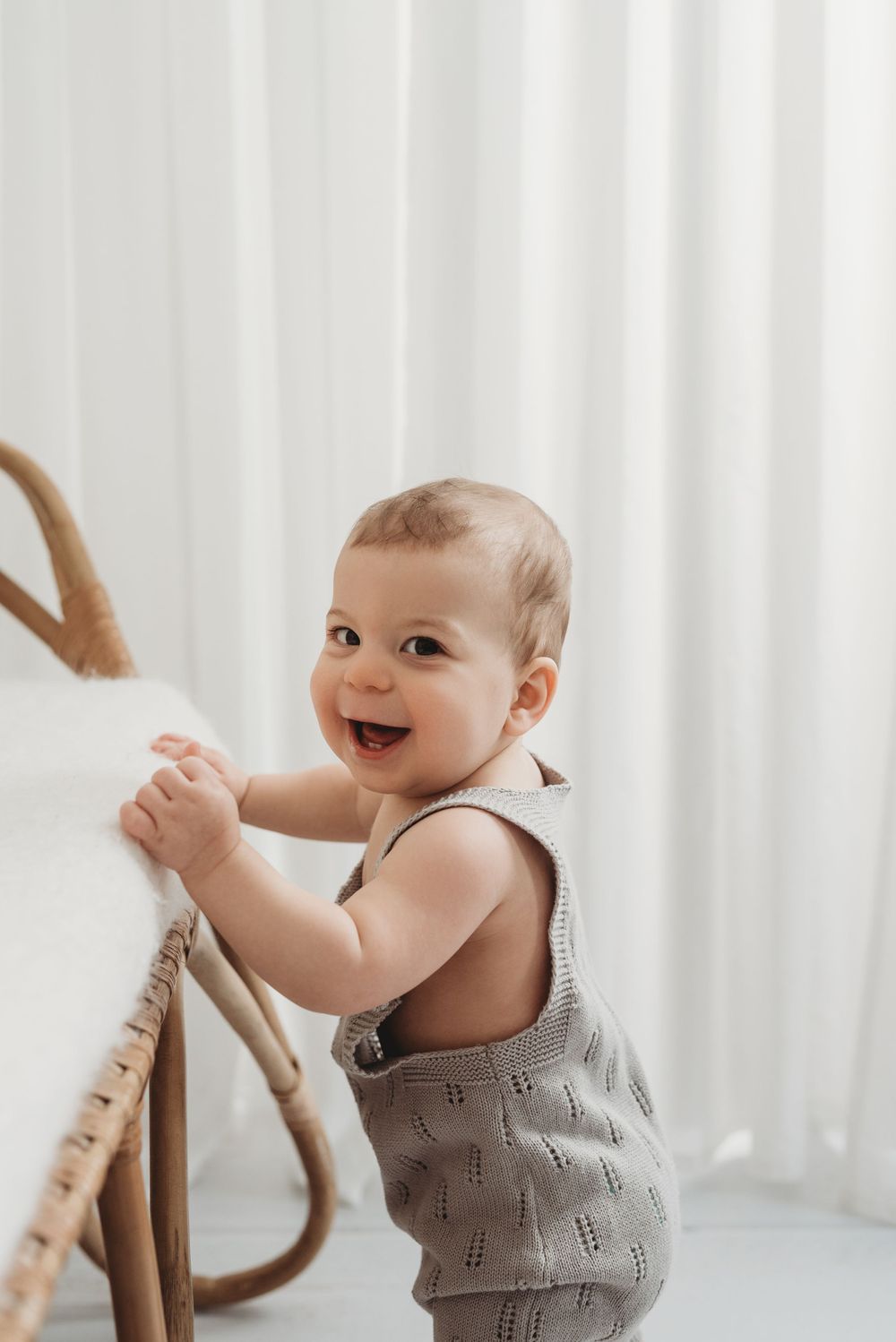 8 month old baby boy standing and holding onto sofa for balance with big smile on his face