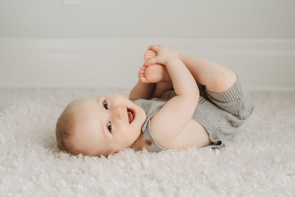 Baby boy smiling holding his feet in happy baby pose at studio milestone session in Toronto