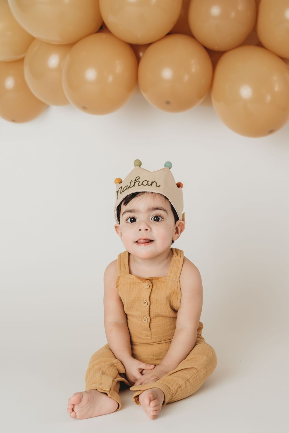 1 year old boy wearing crown in front of balloon backdrop