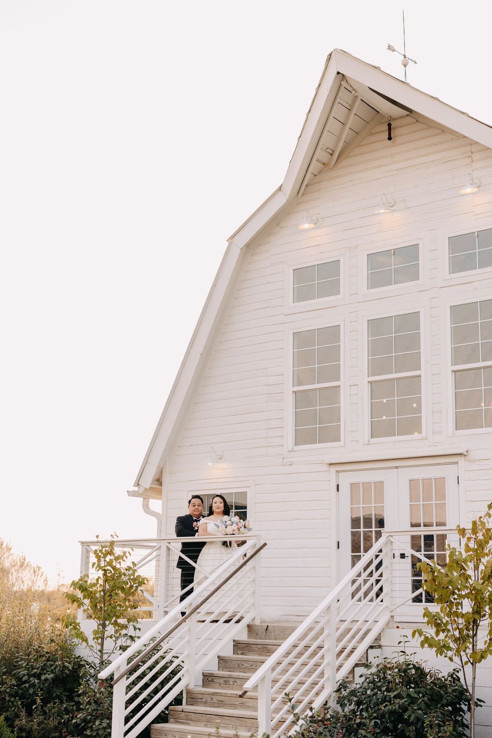 A couple shares a romantic moment on the stairs of a white barn wedding venue.