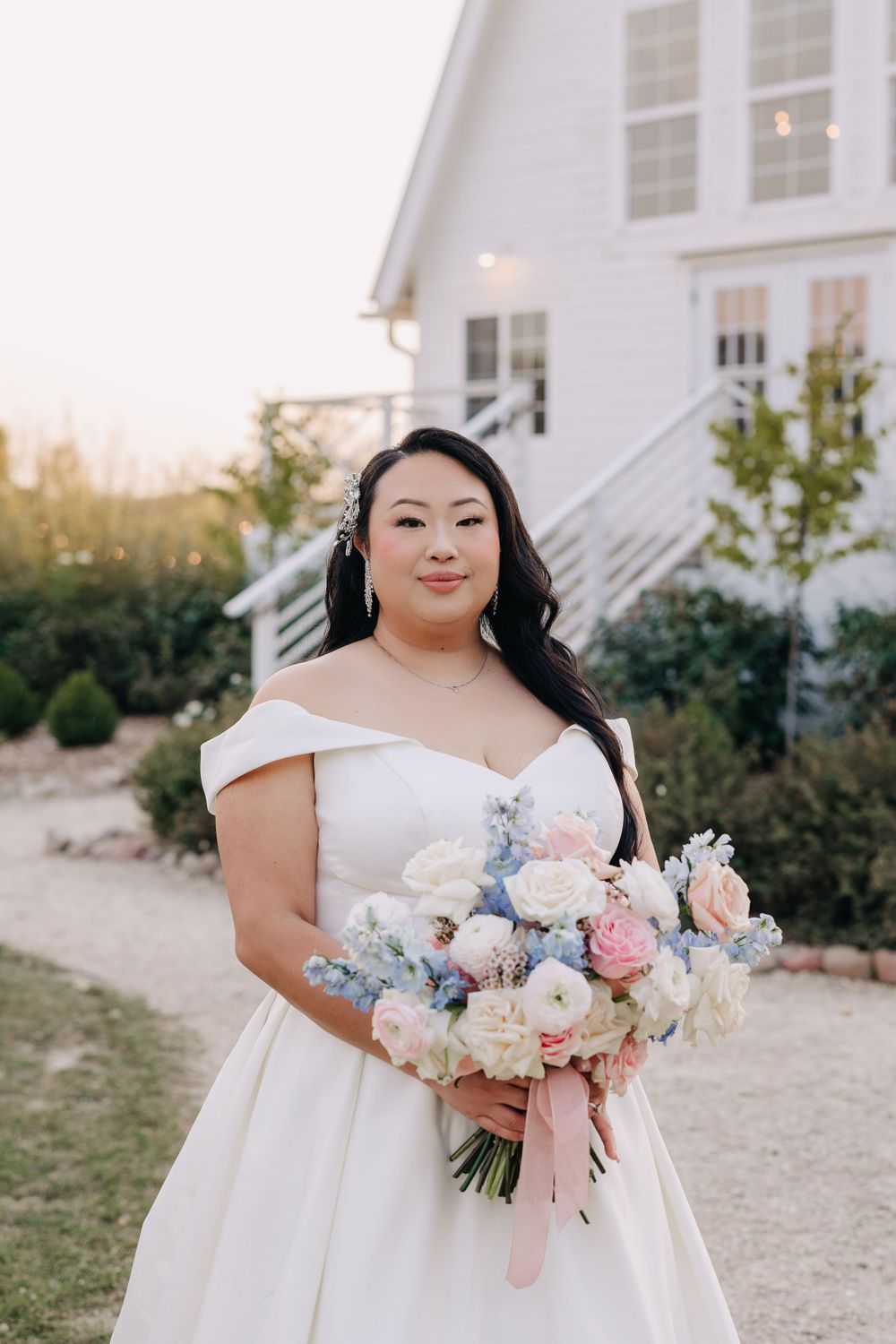 Bride holding a beautiful pastel bouquet with pink and blue flowers outside a white building.