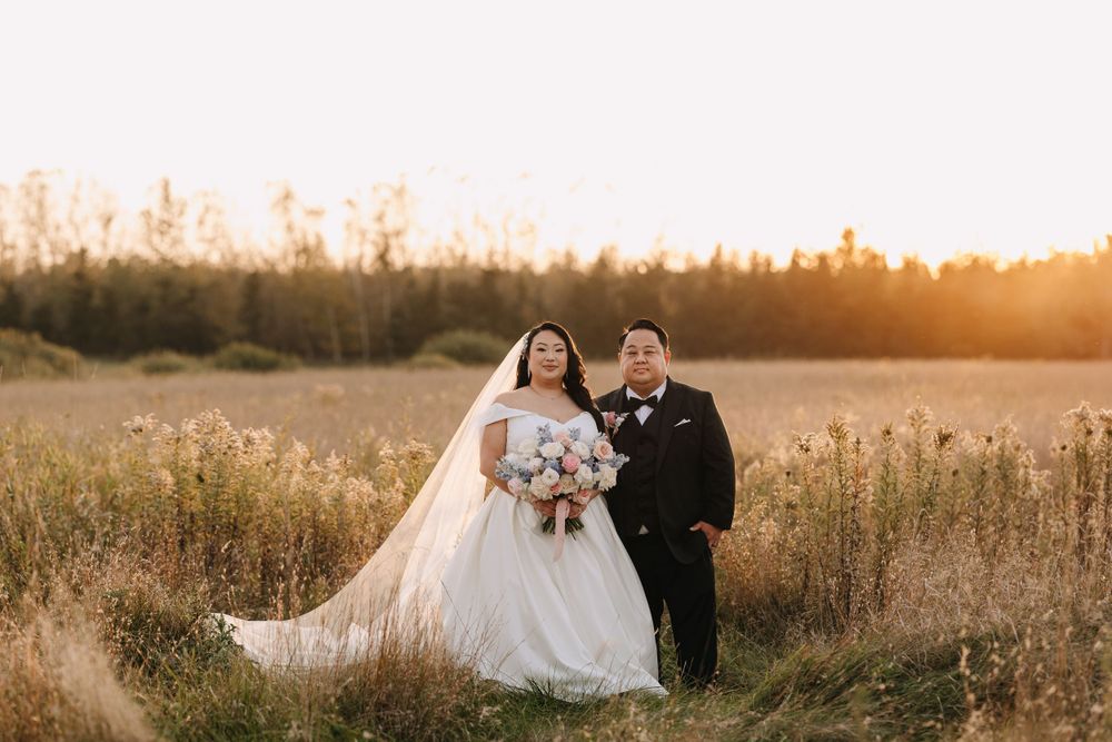 A wedding couple poses in a golden field at sunset with a flowing white dress and black suit.