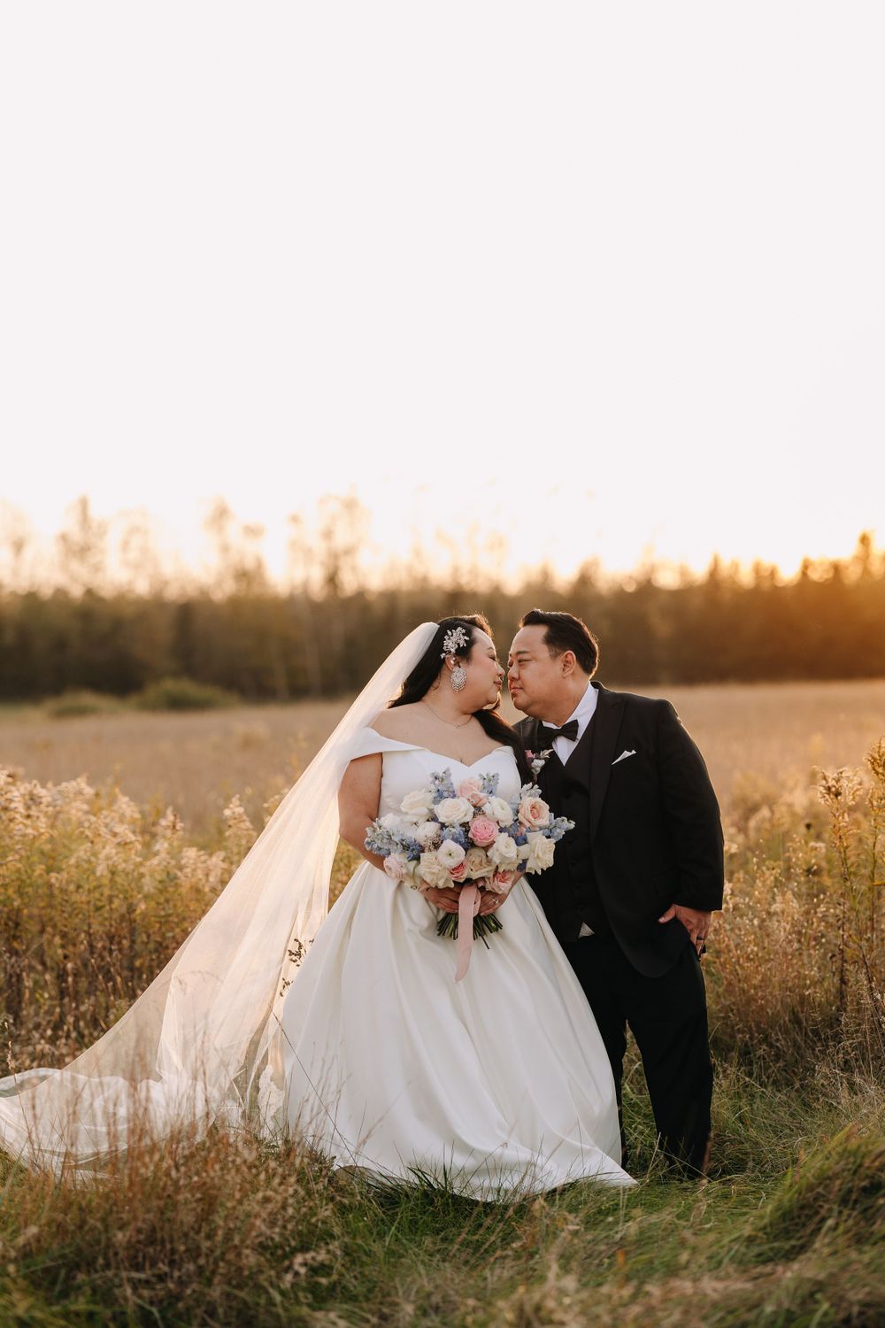 Newlyweds share an intimate moment in a rustic field during golden hour.