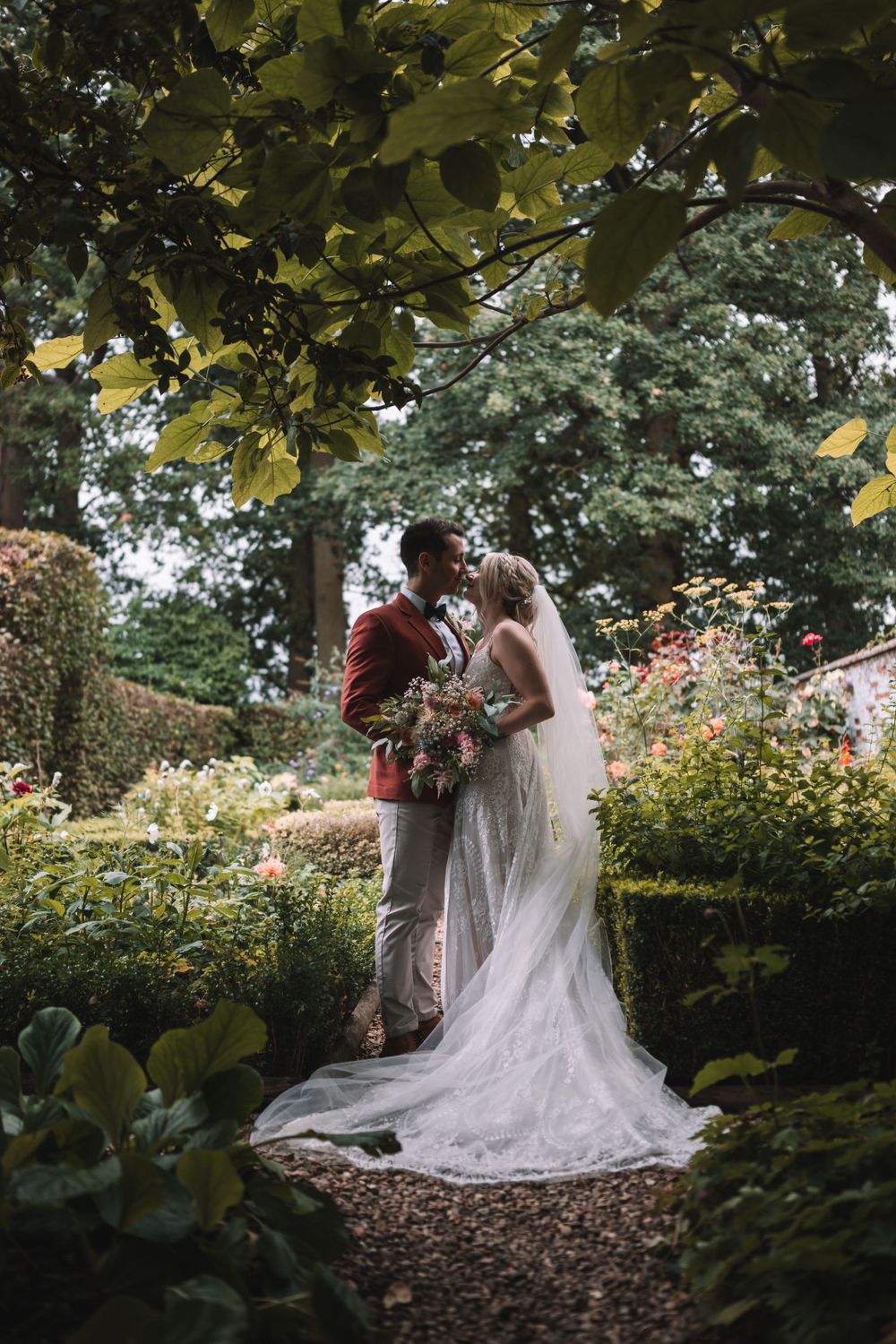 A romantic wedding couple shares an intimate moment in a lush garden setting with flowing white dress and autumn foliage.