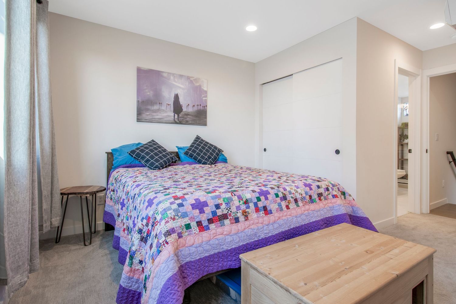 Bedroom with purple themed decor, colorful bedspread, and modern side table.