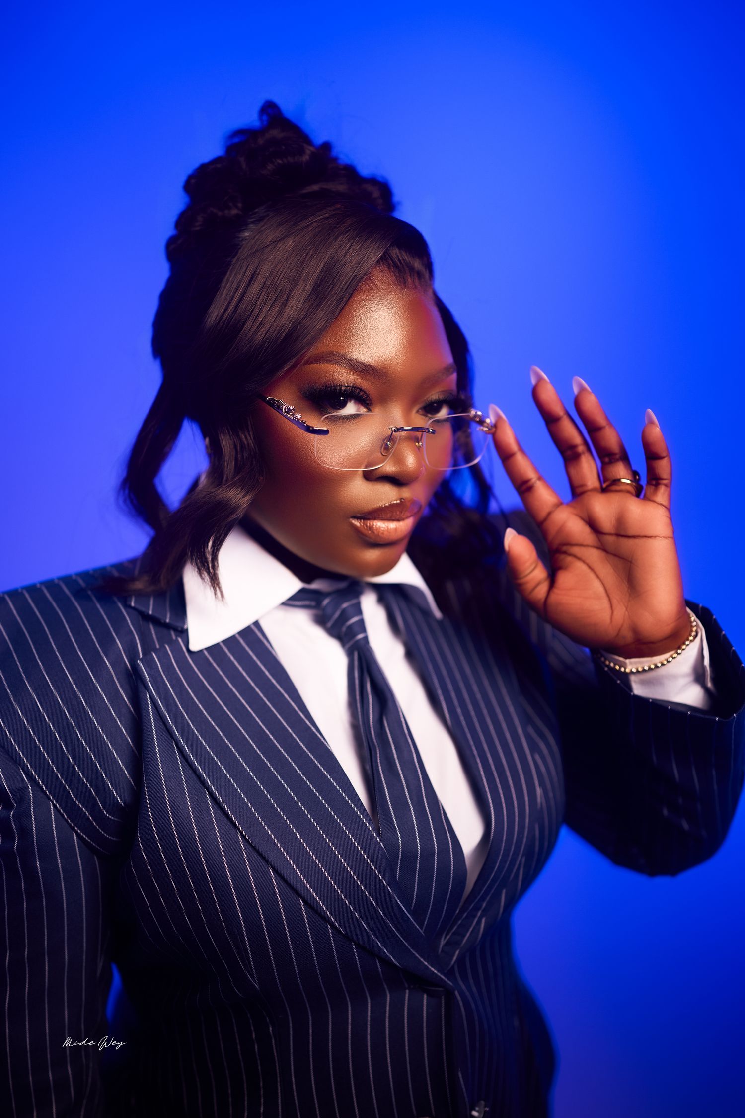 Professional portrait against blue background featuring pinstripe suit, white collar shirt and tie with stylish glasses.