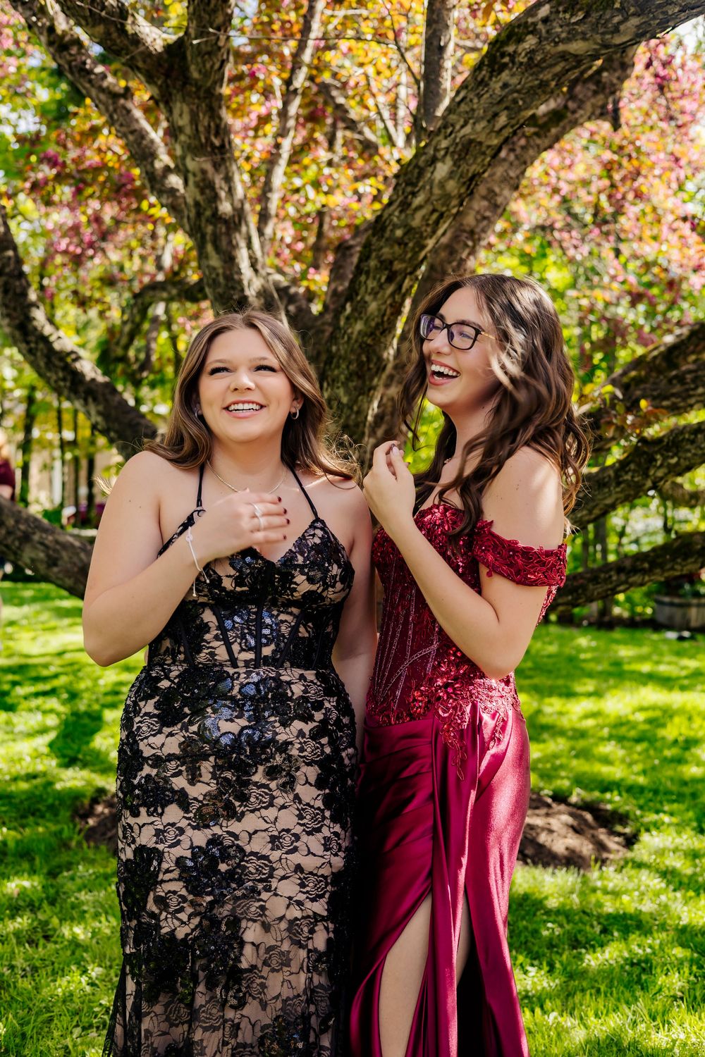 prom photo, two girls one in a red dress the other in a black dress, with a big tree behind them