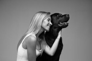 A person in a white tank top embraces a black dog in a minimalist black and white portrait.