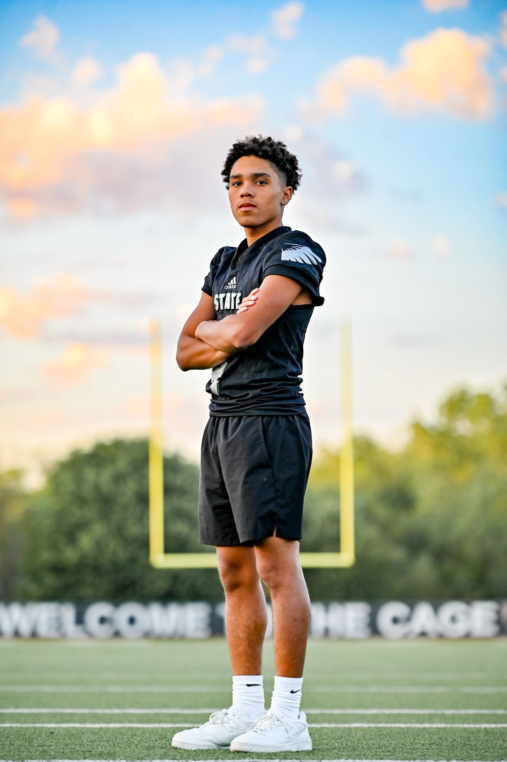 Football player stands confidently on field with goal post visible at sunset.