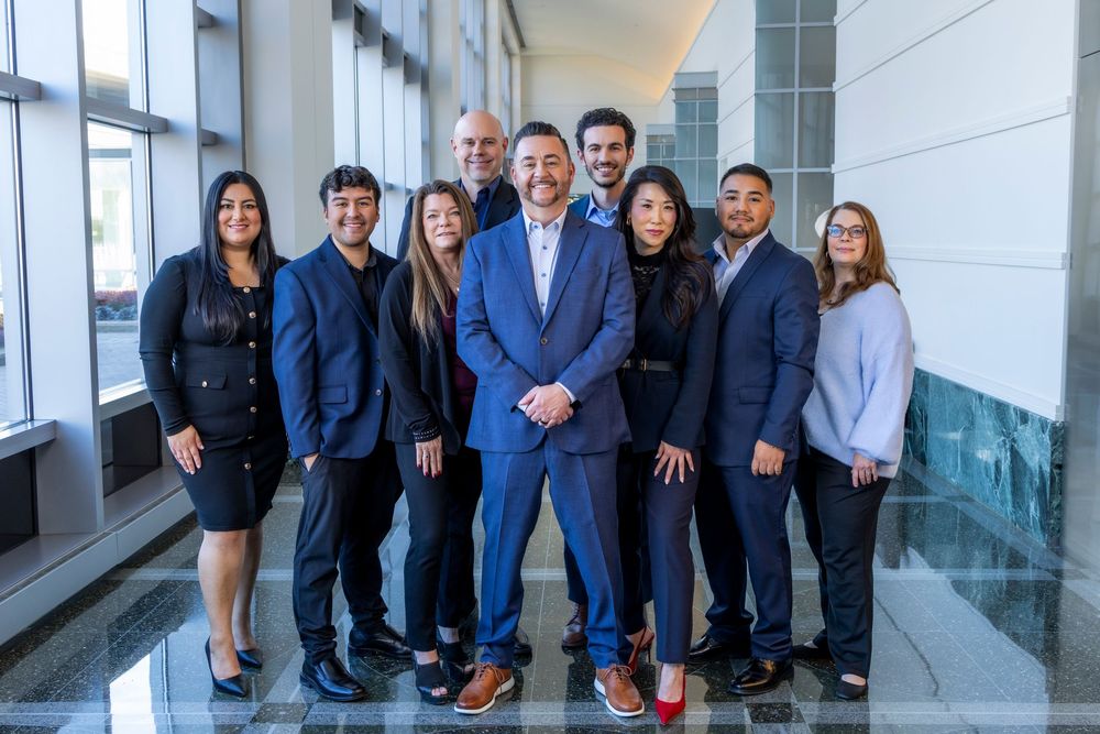 A group of professionally dressed business people stand together in a modern office hallway.