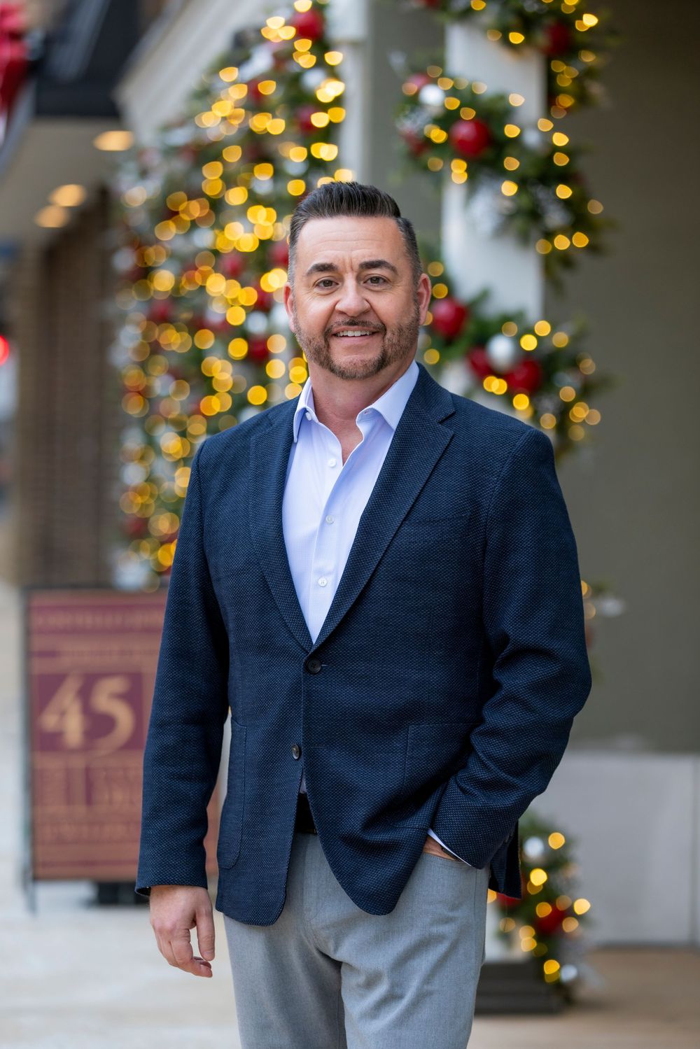 Professional headshot portrait in front of holiday decorations with warm bokeh lights in the background.