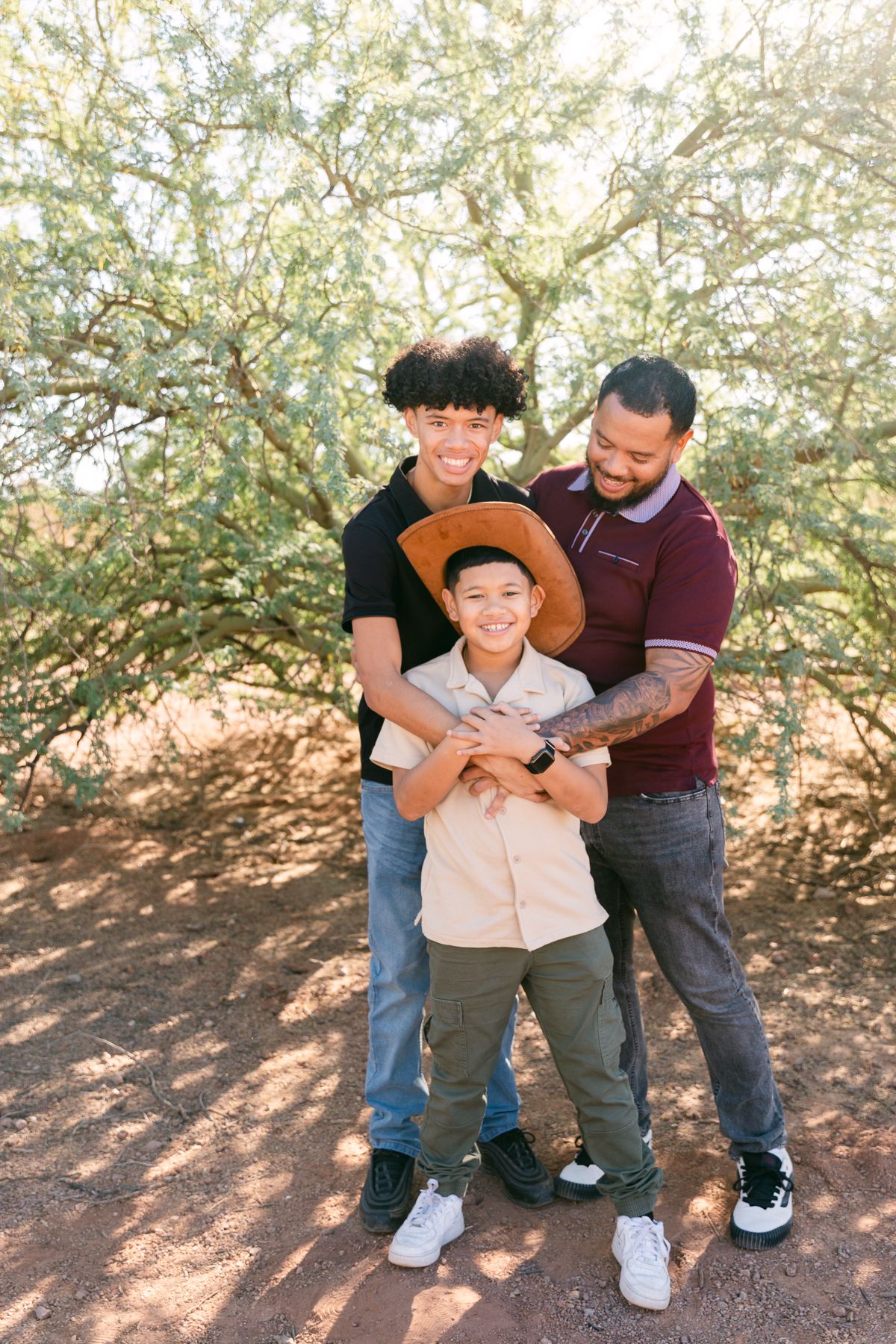 Two boys and a man are laughing. One boy is wearing a cowboy hat, the other is wearing a black shirt and the man is in a red shirt