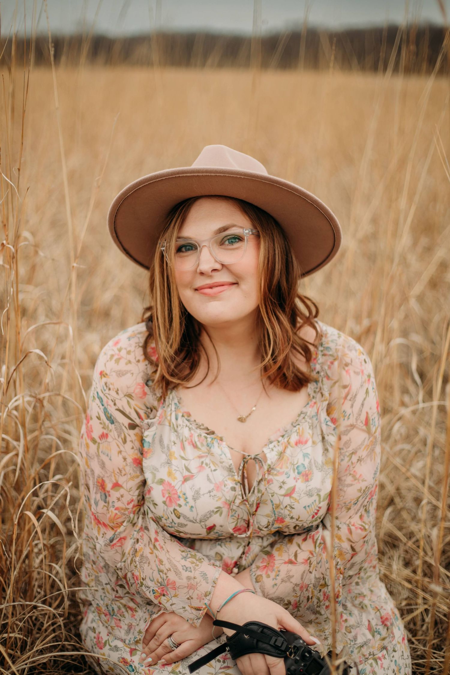 A person in a floral dress stands joyfully in a golden field under overcast skies.