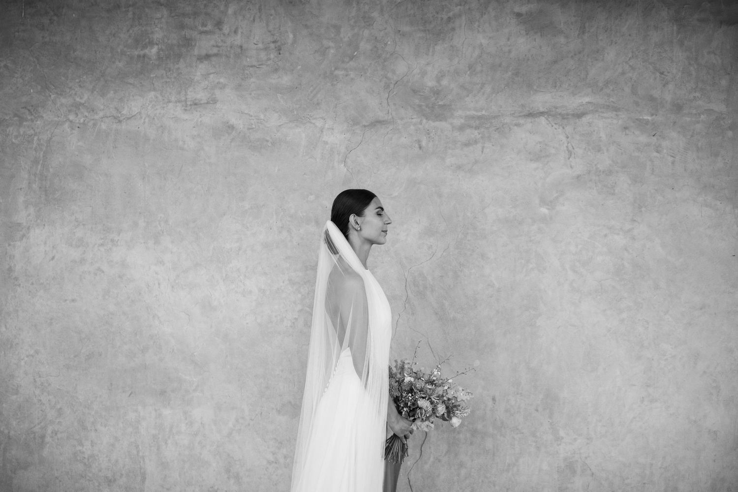 A bride in a white wedding dress walks through an elegant venue with textured walls and dramatic lighting.