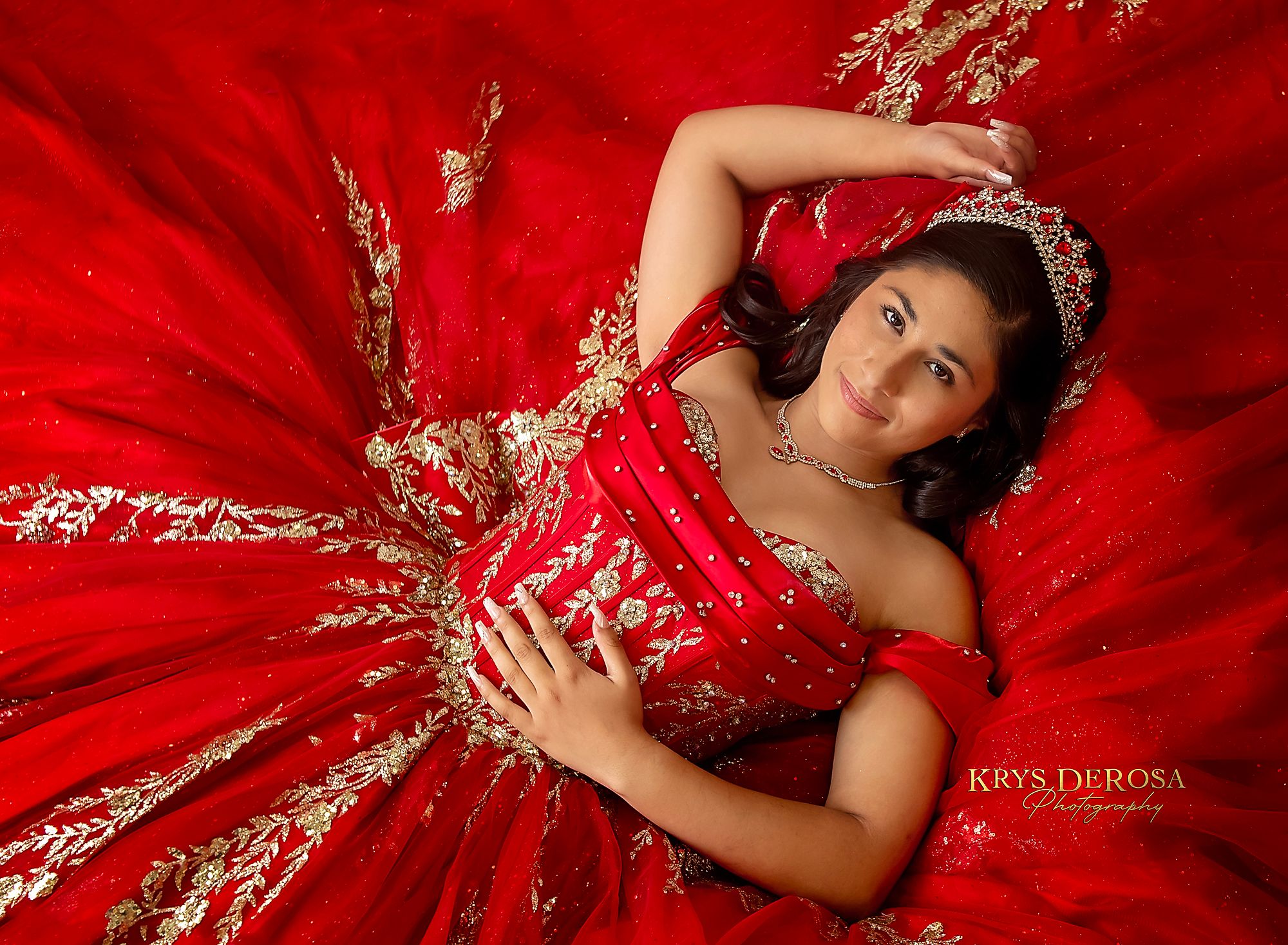 A woman in a glamorous red ball gown with golden embellishments poses elegantly against a dark backdrop.