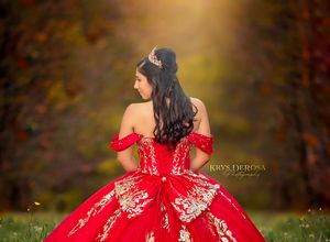 A teenage girl in a vibrant red and gold quinceañera gown stands gracefully in an autumn forest setting.