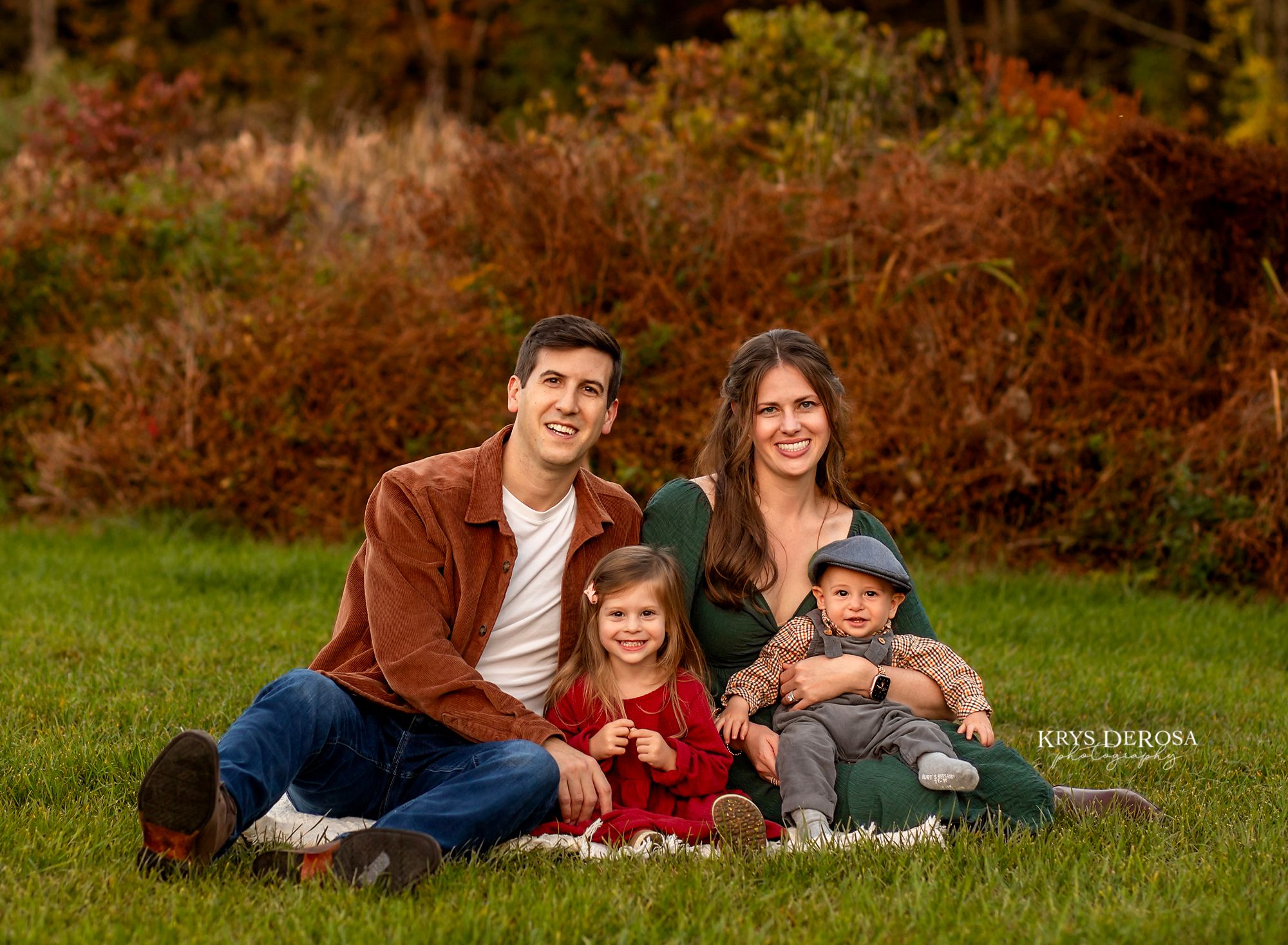 A group of people laying together on grass in a casual outdoor photo session.