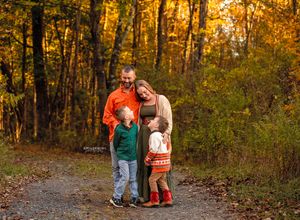 Family of four posing on a forest path surrounded by vibrant autumn foliage during a fall photo session.