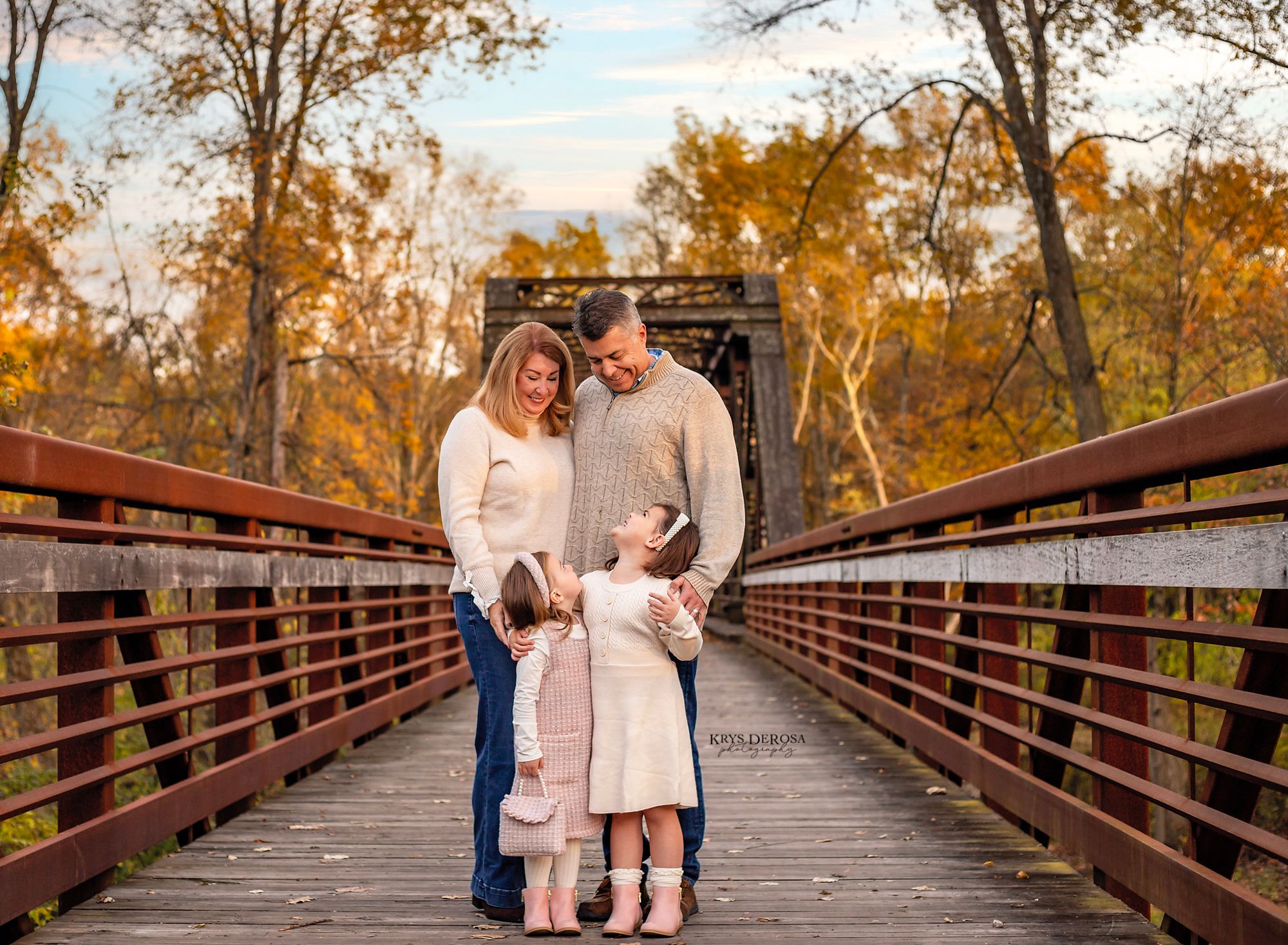 Family of four posing on a wooden bridge surrounded by autumn foliage during a fall photo session.